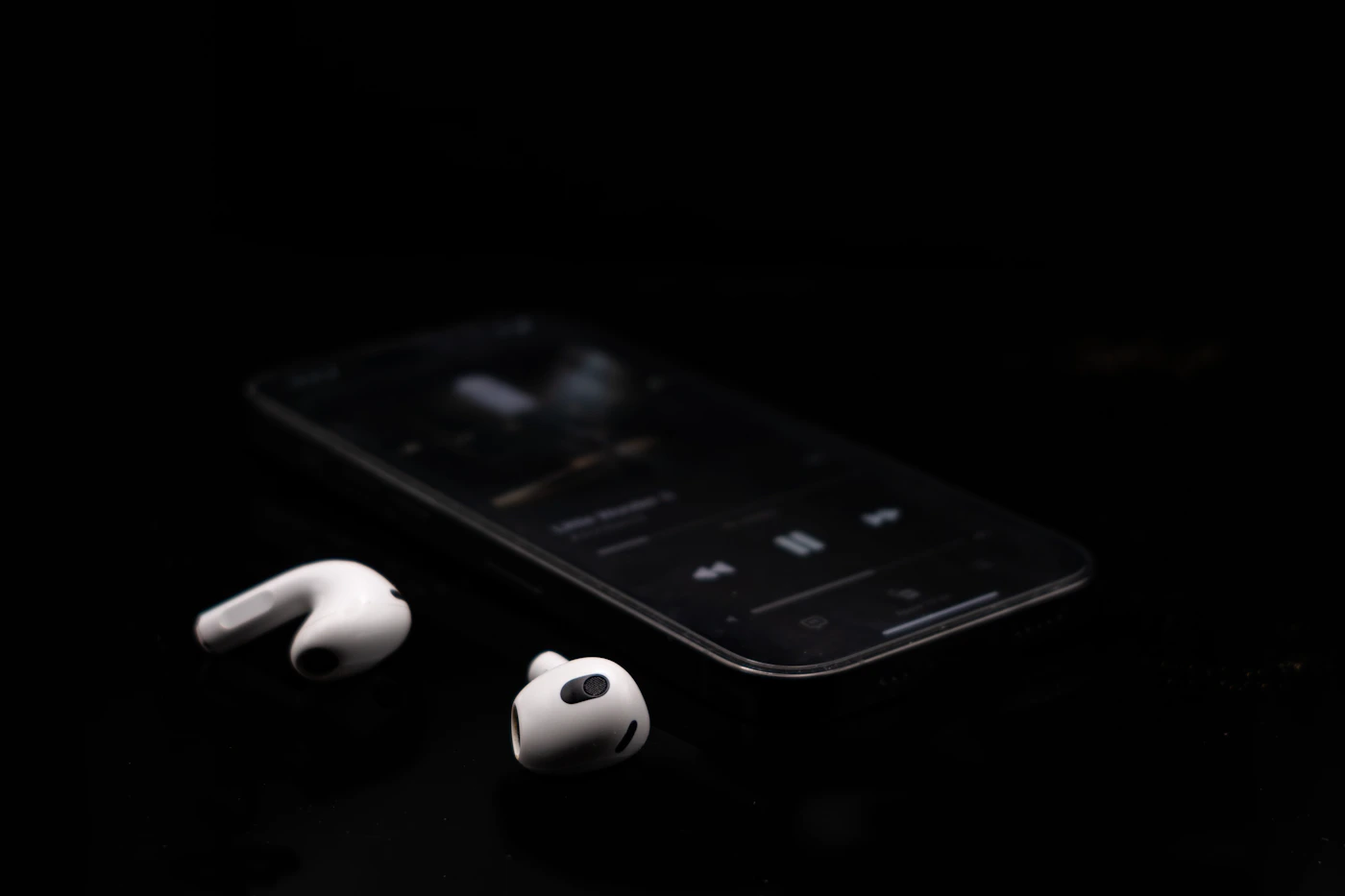 A smartphone and wireless earphones on a dark surface